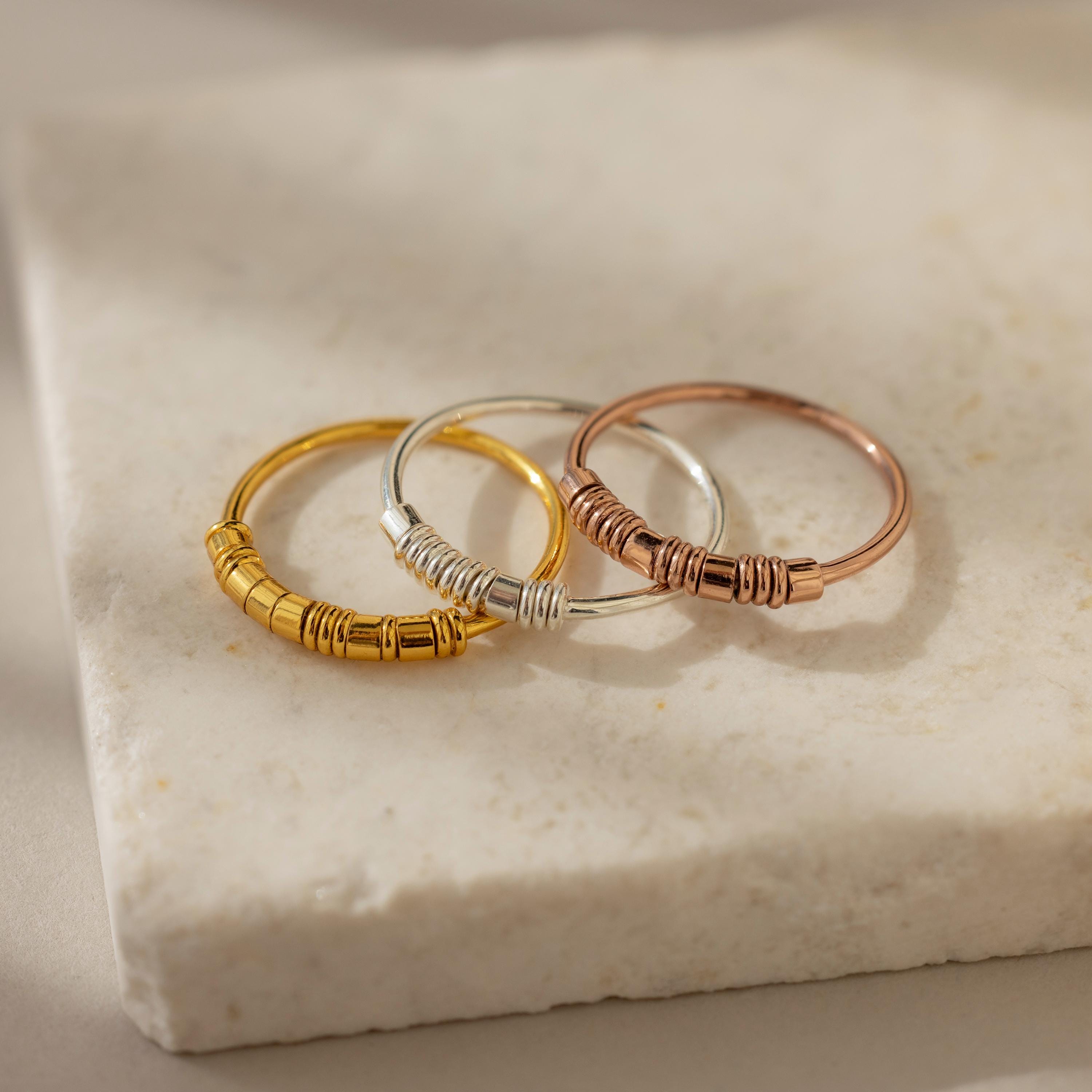 Three dainty beaded rings made of sterling silver, with one ring featuring gold plating, displayed on a stone surface.